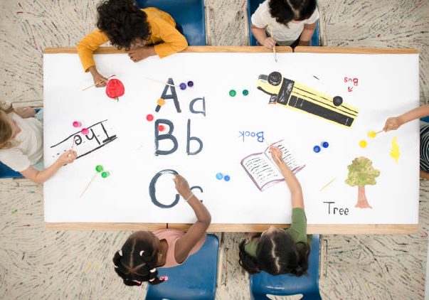 An aerial shot of multi ethnic preschool children drawing on a giant doodle pad.